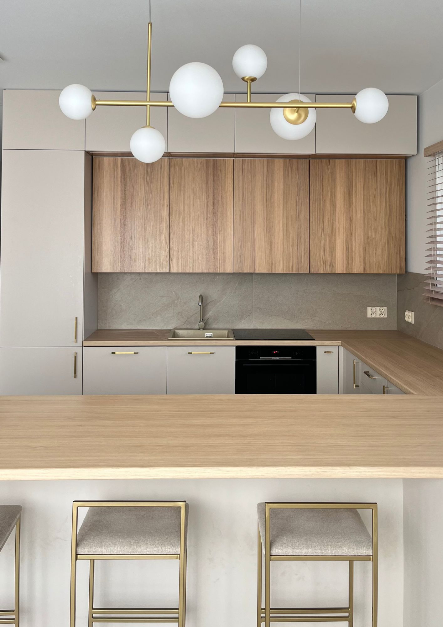 A modern, custom-built kitchen with beige cabinet fronts, wood accents, and gold handles is the perfect fit for elegant interior