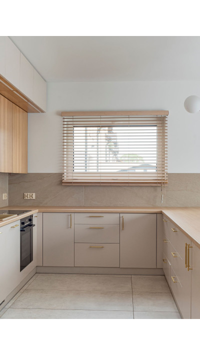 Minimalistyczna kuchnia na wymiar Leszno – drewniany blat, beżowe fronty i nowoczesny design.