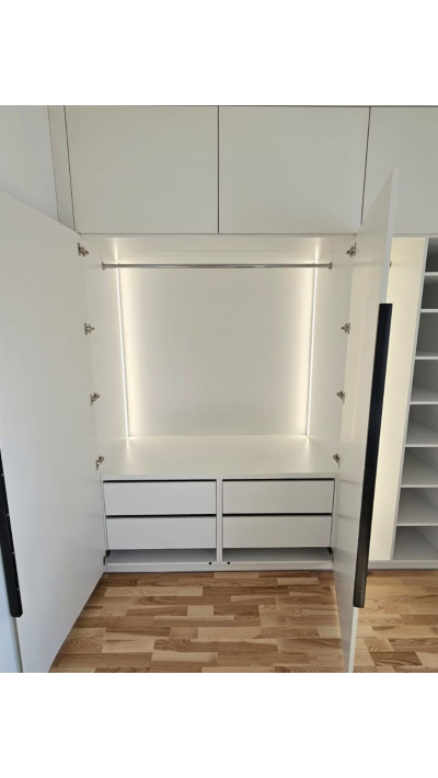 A built-in closet with smooth fronts and black handles—a modern, floor-to-ceiling unit. A built-in closet with smooth fronts and black handles—a modern, floor-to-ceiling unit.