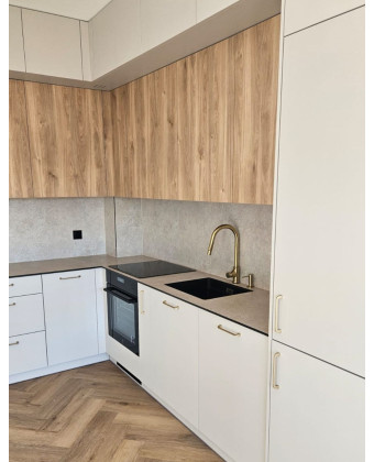 A modern kitchen in warm shades of wood and beige, with matte cabinet fronts and gold handles, featuring a black sink and faucet