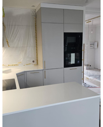 A modern kitchen in matte gray with a white countertop and gold handles