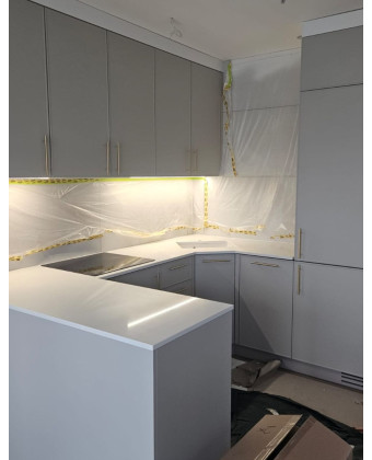 A modern kitchen in matte gray with a white countertop and gold handles
