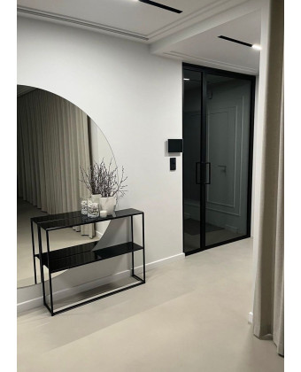 A slim ZENOBIA console table made of black glass and metal in a modern entryway